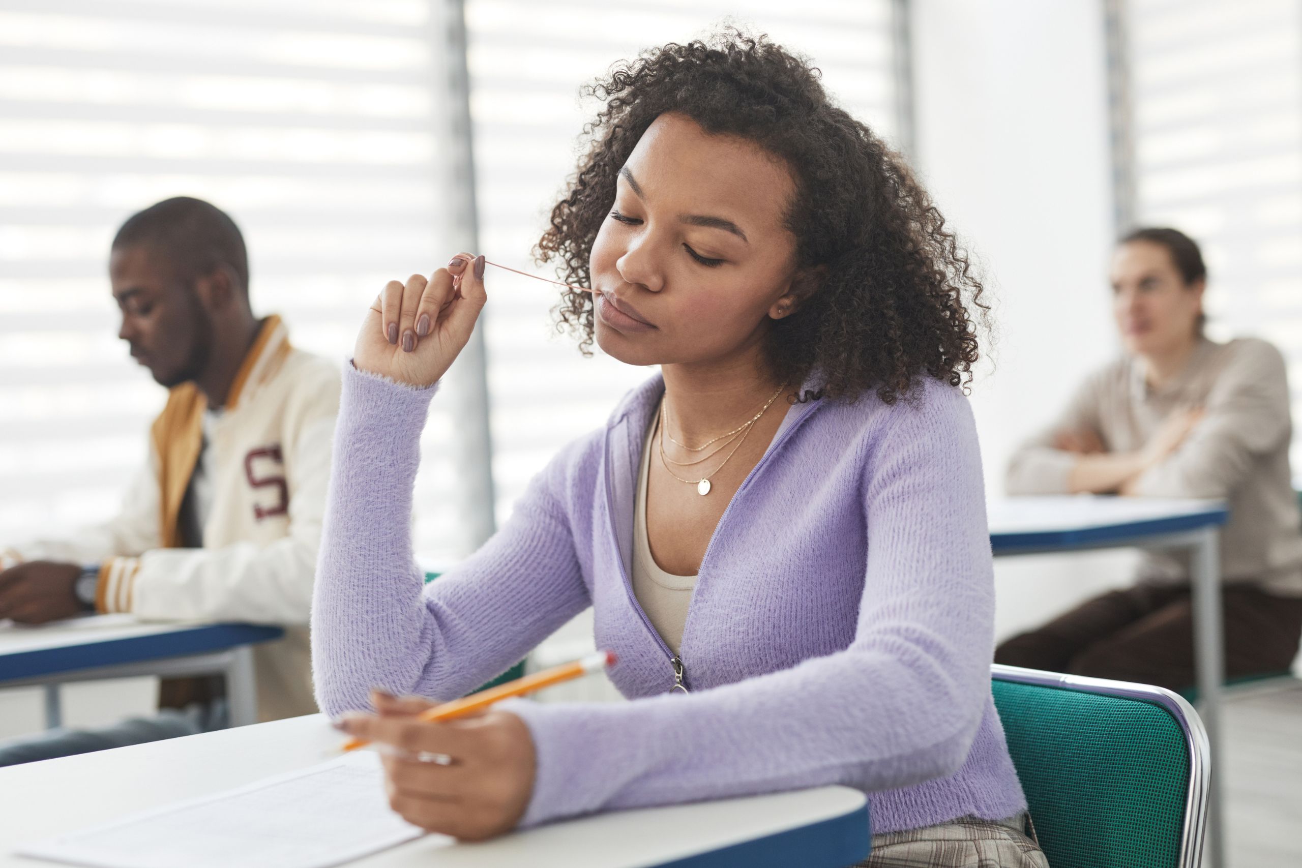 Student in classroom holding pencil thoughtfully during SAT or ACT exam
